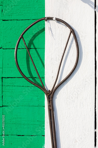 Old metal carpet beater hangs on green and white wall of wooden house