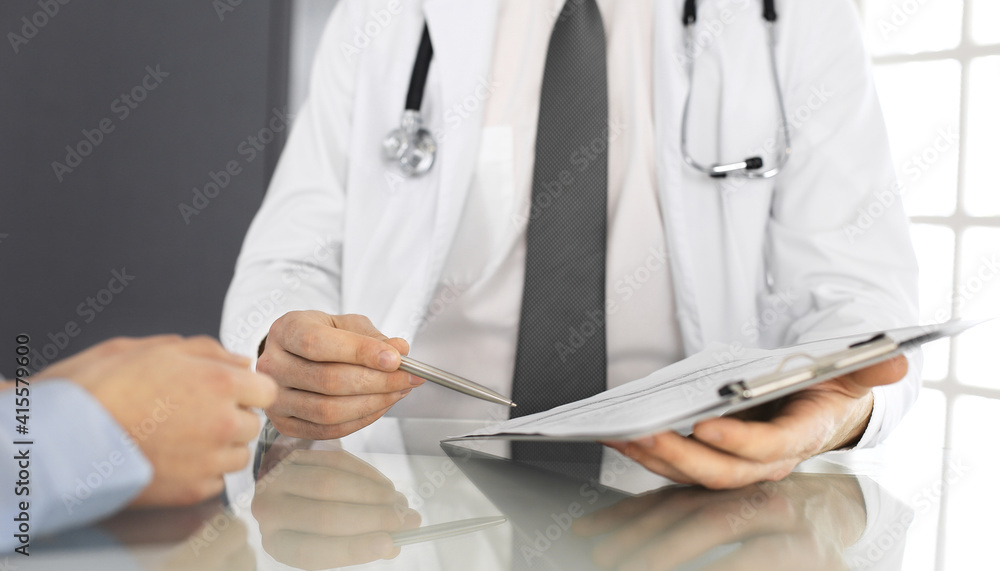 Unknown male doctor and woman-patient discussing current health examination while sitting in clinic and using clipboard. Good medical service in hospital. Medicine concept Unknown male doctor and woman-patient discussing current health examination while sitting in clinic and using clipboard. Good medical service in hospital. Medicine concept