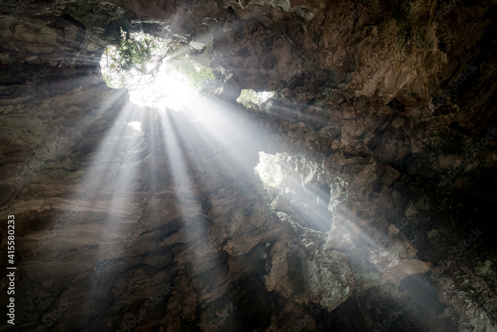 Upward shot of light rays entering a deep cave and illuminating the surrounding stone walls Upward shot of light rays entering a deep cave and illuminating the surrounding stone walls