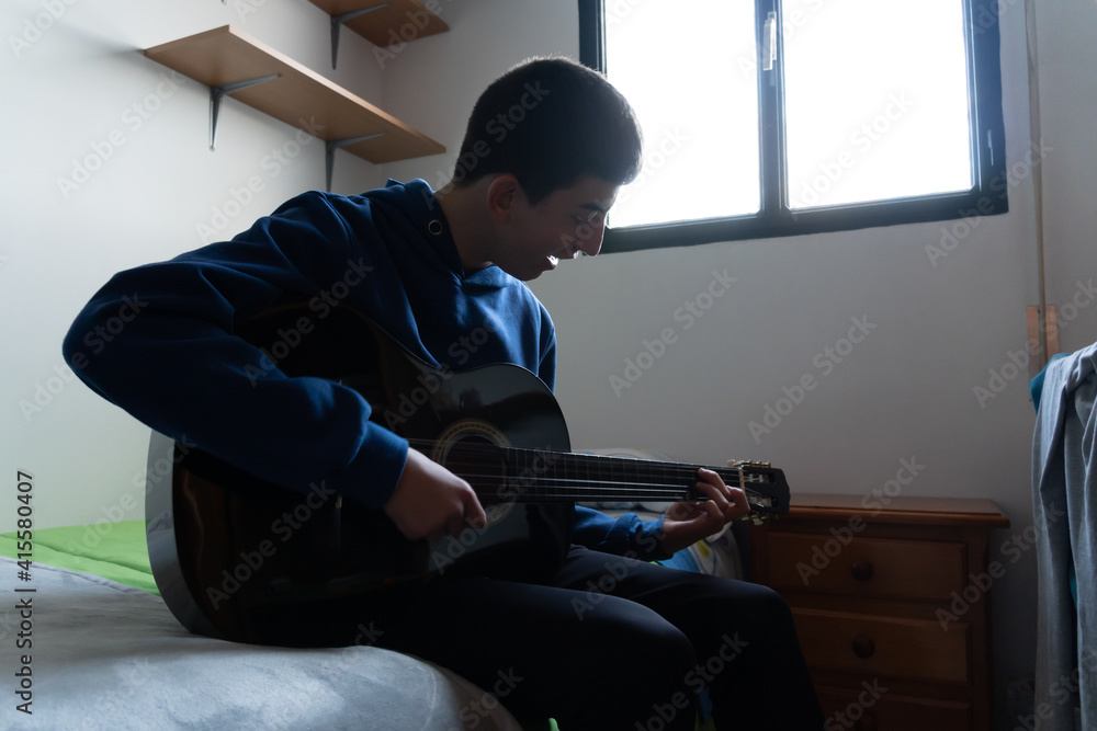 Stock photo of young boy playing his guitar in the bedroom.