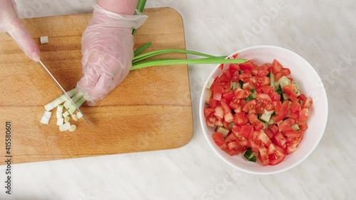Vegetable salad. Chop fresh green onions on a wooden board. Chef's hands in gloves. top view