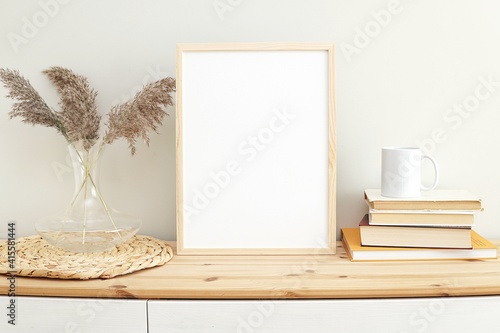 Wooden frame mockup for wall art, boho style living room interior, books and coffee cup on shelf.