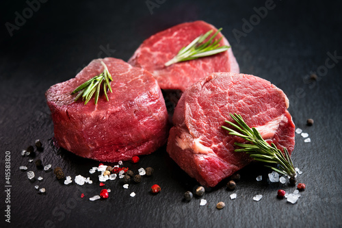 Foto Raw beef filet mignon steaks with rosemary, pepper and salt on dark rustic board