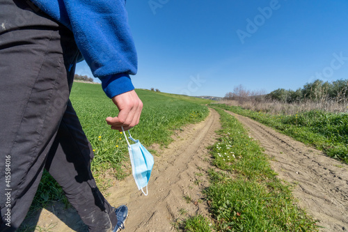 Unrecognized young boy wearing sports clothes and holding face mask walking in the countryside.