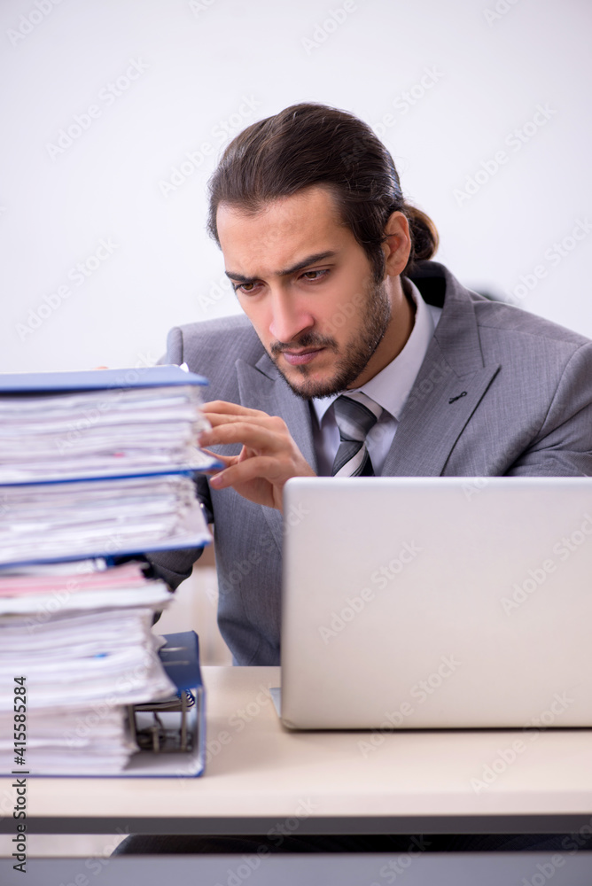 Young male employee unhappy with excessive work in the office Young male employee unhappy with excessive work in the office