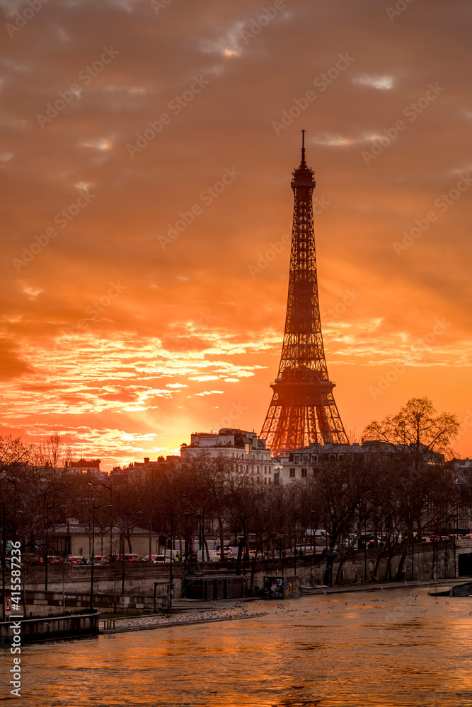Paris, France - February 12, 2021: CItyscape of Paris in winter. Ships and brigde over Seine river with Eiffel tower in background and dramatic cloudy sky