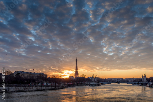 Paris, France - February 12, 2021: CItyscape of Paris in winter. Ships and brigde over Seine river with Eiffel tower in background and dramatic cloudy sky