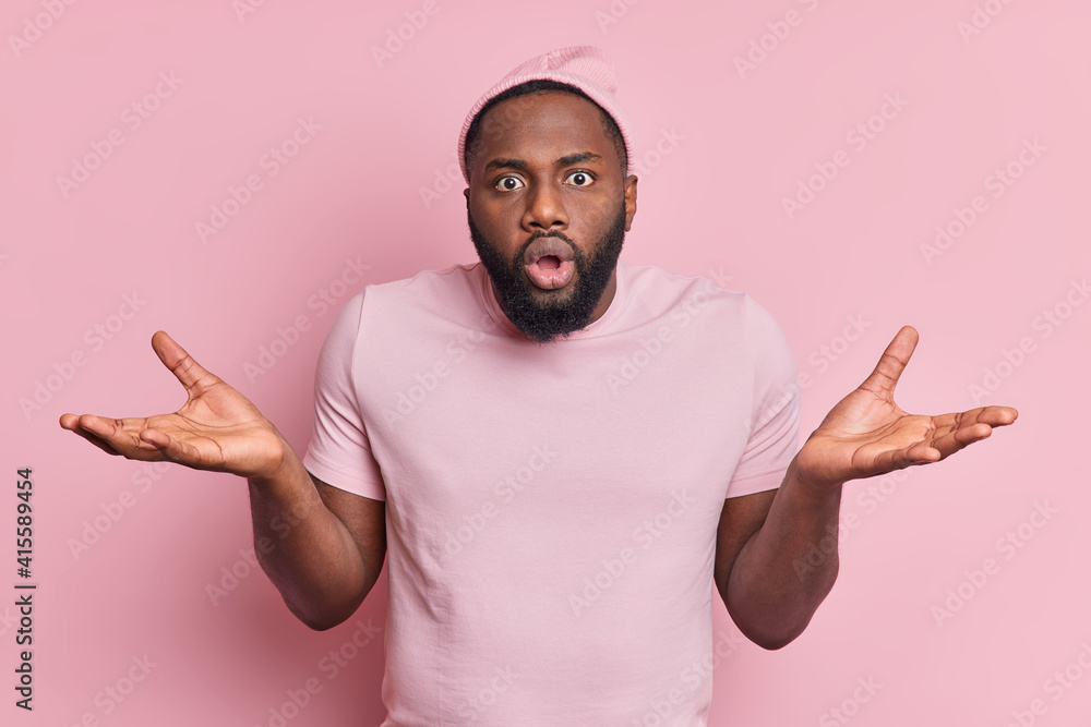 Hesitant confused shocked black man spreads palms puzzled by difficult situation looks surprised and unaware wears hat t shirt isolated over pink background. People doubt bewilderment concept Hesitant confused shocked black man spreads palms puzzled by difficult situation looks surprised and unaware wears hat t shirt isolated over pink background. People doubt bewilderment concept