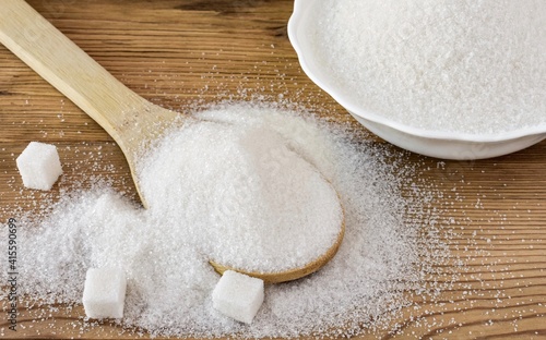 Bowl and wooden spoon with white granulated sugar and sugar cubes on a wooden background. Close up.