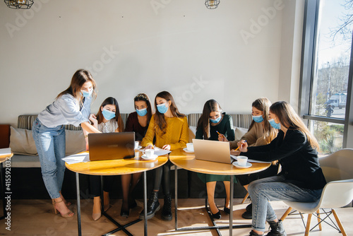 A group of girls in masks sit in a cafe and work on laptops. Teaching students.