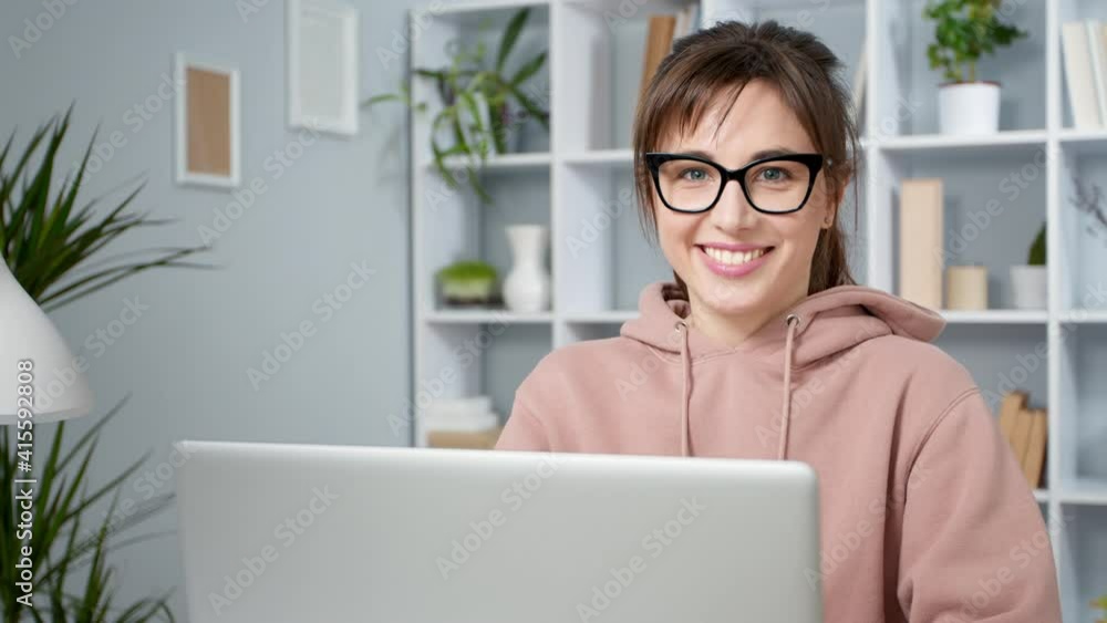 Portrait of a happy young woman working on a laptop at home. Smiling female student with glasses looking at the camera. Portrait of a happy young woman working on a laptop at home. Smiling female student with glasses looking at the camera.