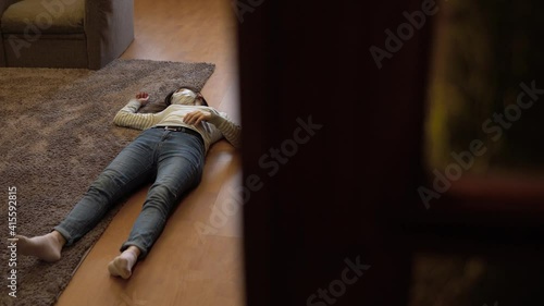 A young woman lies on the floor dead. A woman in a medical mask lies unconscious on the floor. The view from the door.