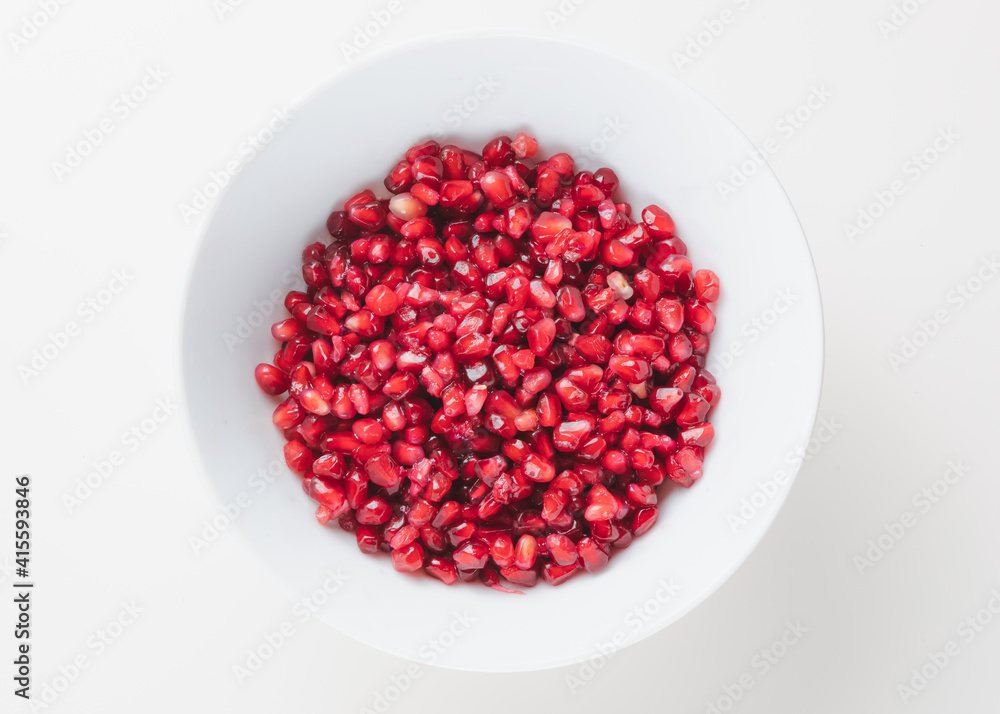 Overhead view of superfood pomegranate seeds in a white bowl on a plain white surface and background.