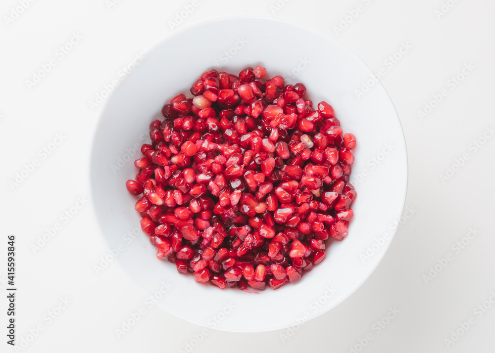 Overhead view of superfood pomegranate seeds in a white bowl on a plain white surface and background. Overhead view of superfood pomegranate seeds in a white bowl on a plain white surface and background.