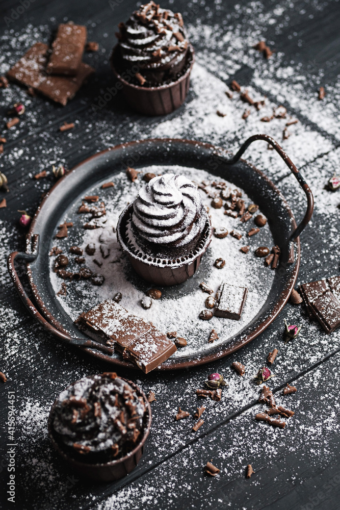 Several muffins or cupcakes with chocolate shaped cream at black table. Powdered sugar is scattered over the cakes Several muffins or cupcakes with chocolate shaped cream at black table. Powdered sugar is scattered over the cakes