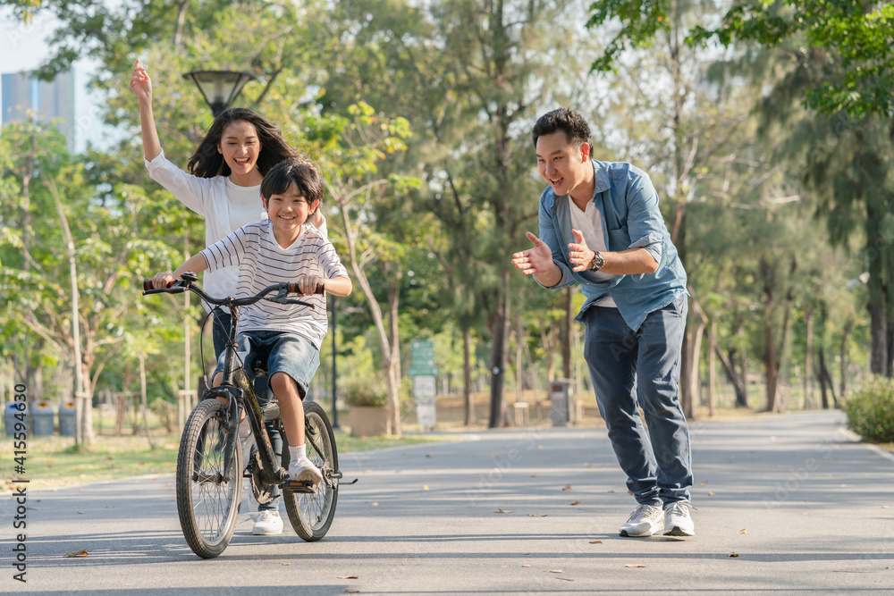 Happy Asian family father and mother teaching their son to ride bicycle at the park Happy Asian family father and mother teaching their son to ride bicycle at the park