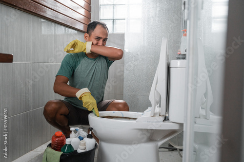 Foto Sad man wearing gloves over his nose cleaning smelly toilets in the bathroom