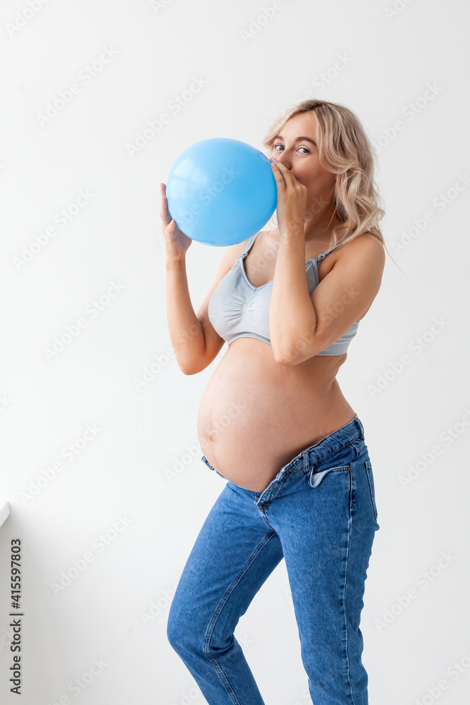 A beautiful young pregnant woman with a big belly in blue jeans holds a balloon that means that a boy will be born. A beautiful young pregnant woman with a big belly in blue jeans holds a balloon that means that a boy will be born.