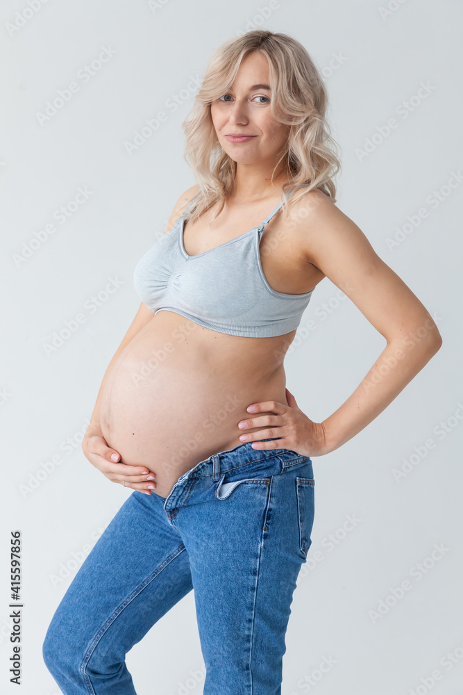 beautiful young pregnant blonde woman in blue jeans and a top for feeding a baby stands and strokes a big belly. beautiful young pregnant blonde woman in blue jeans and a top for feeding a baby stands and strokes a big belly.