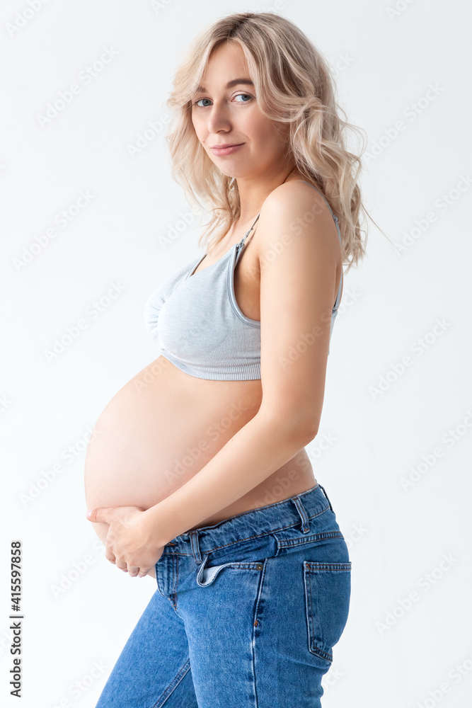 beautiful young pregnant blonde woman in blue jeans and a top for feeding a baby stands and strokes a big belly. beautiful young pregnant blonde woman in blue jeans and a top for feeding a baby stands and strokes a big belly.