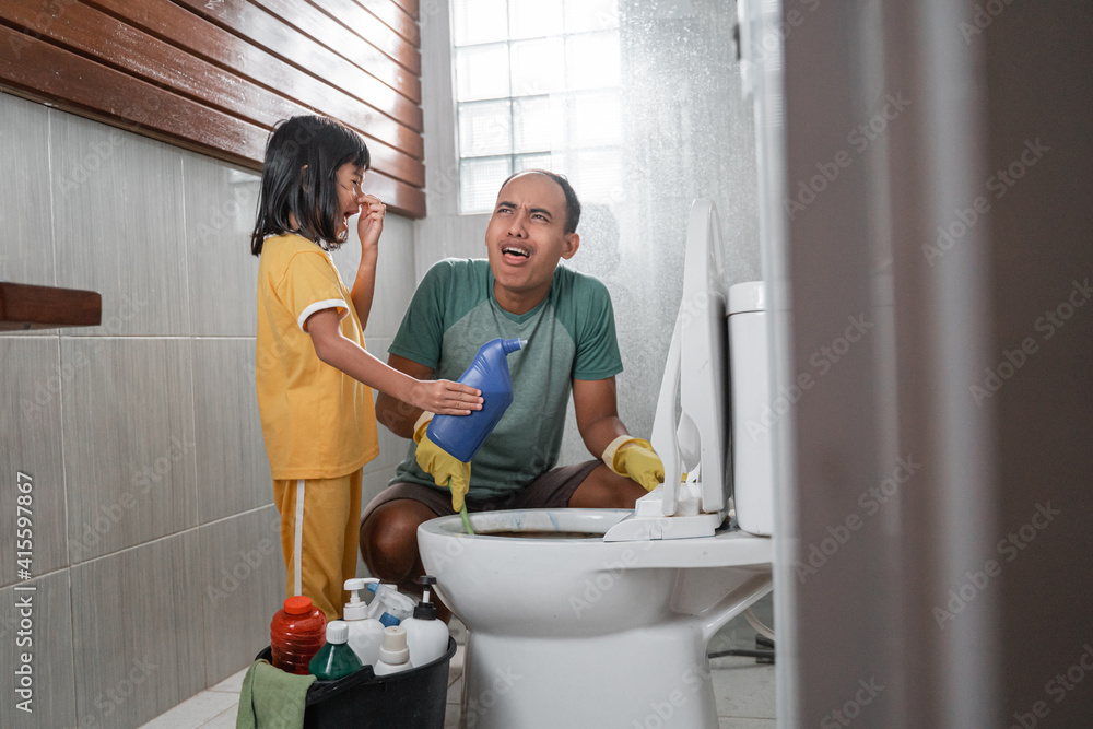 Obraz premium the little girl in a nasty pose holding a bottle of cleaning fluid chatting with her dad while brushing the dirty toilet in the bathroom