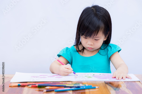 Pupils girl are concentrating on drawing and painting with colored pencils crayon on art paper book. Asian little child learning at home. Children aged 3-4 years old. Isolated wall white background.