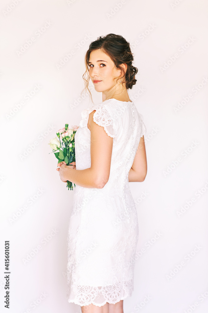 Portrait of young pretty woman wearing white dress, holding flowers, back view Portrait of young pretty woman wearing white dress, holding flowers, back view