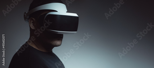 Close-up of a man in his thirties wearing virtual reality glasses on a dark background. Concept of artificial intelligence, hacking, fraud. Copy space