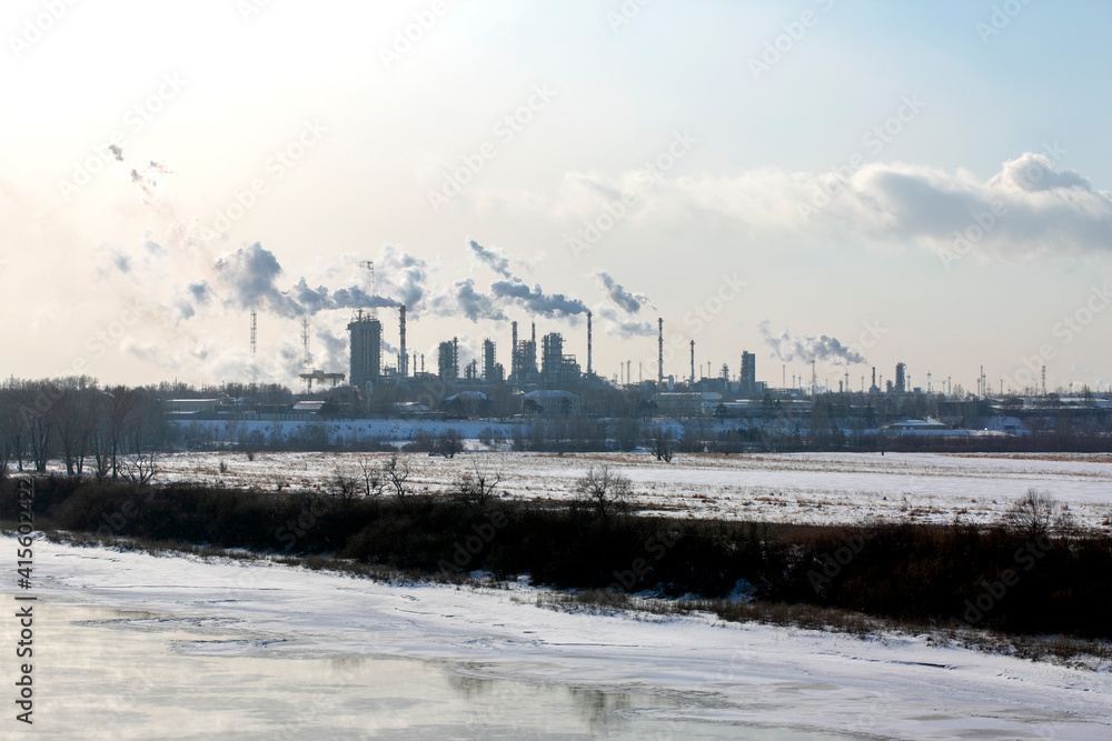 
An industrial plant is on the horizon. Smoking chimneys of a plant on a winter day. Against the background of a frozen river