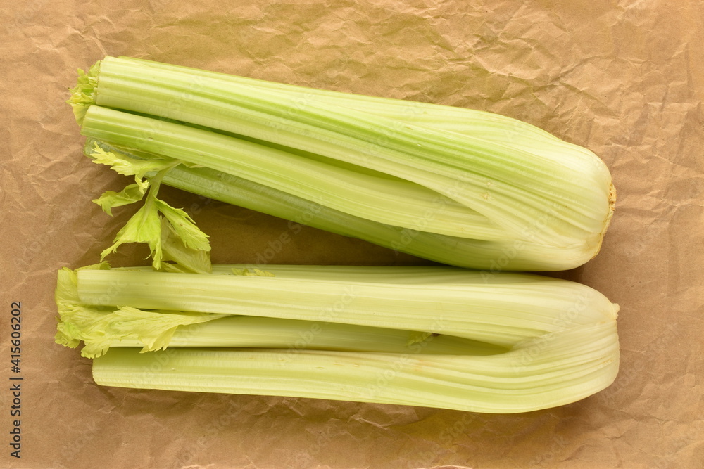 Two light green natural, juicy stalks of celery on brown paper, close-up, top view. Two light green natural, juicy stalks of celery on brown paper, close-up, top view.