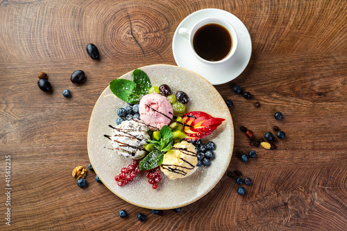 
Ice cream dessert. Three multi-colored balls of ice cream, decorated with fruits, berries and mint, on a large plate 