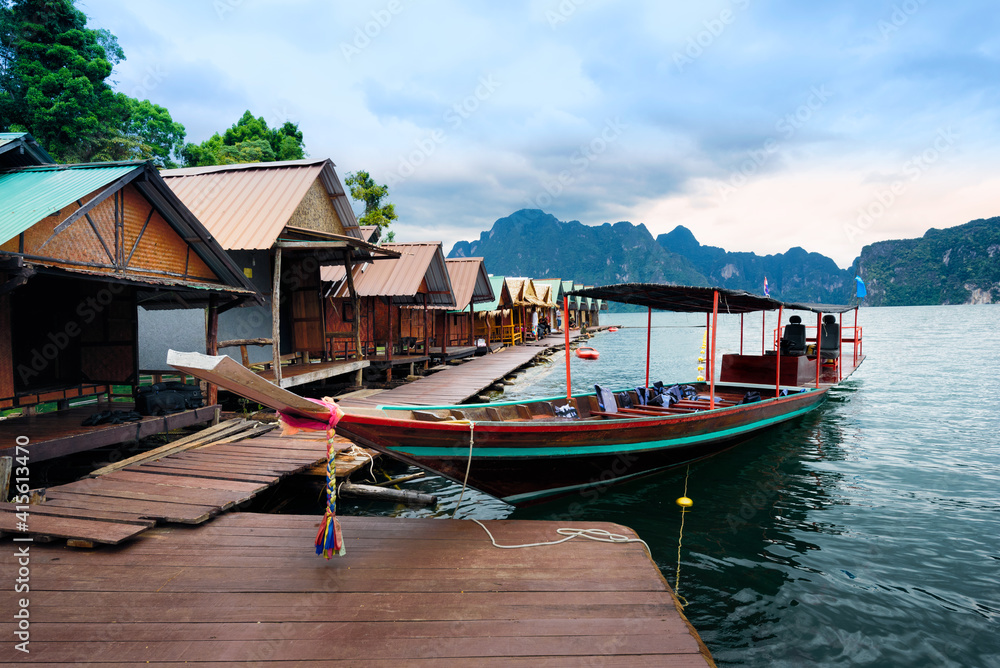 Long-tailed boat floating on the asia lake and Raft house homestay in the among the islands with mountains in background at Surat Thani Province of Thailand.