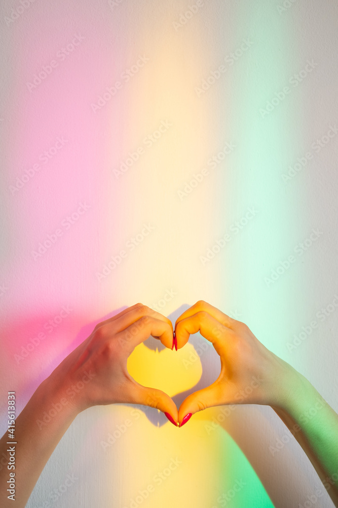 Love sign. Romantic sympathy. Peace hope. Affection desire. Female hands creating heart gesture on wall with blur rainbow overlay glowing lights. Love sign. Romantic sympathy. Peace hope. Affection desire. Female hands creating heart gesture on wall with blur rainbow overlay glowing lights.
