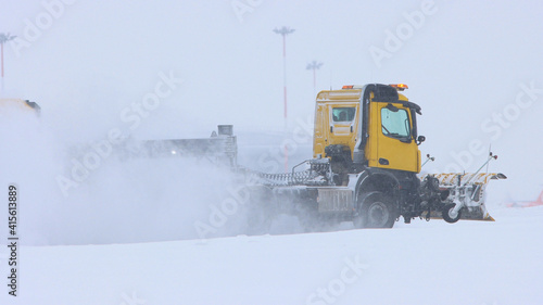 A yellow truck on the snowy airfield cleaning the path