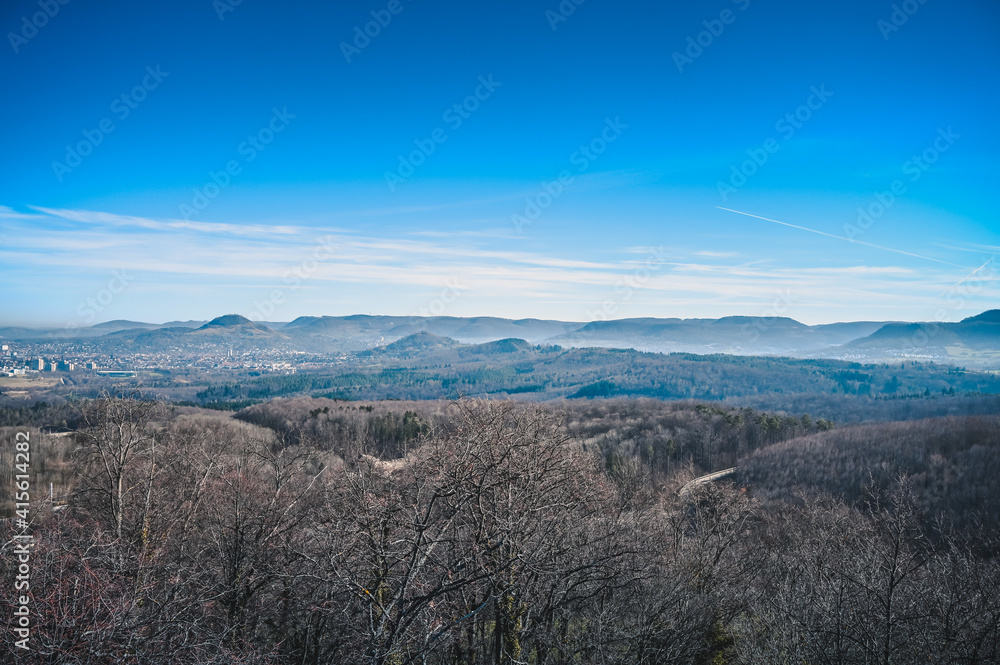Beautiful aerial view of forests in front of the mountain ridges of the Swabian Alb on a sunny winter day without snow.