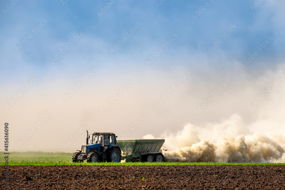 Fototapeta premium Tractor spraying fertilizer on the soil early spring time. Maintaining soil fertility, improving crop development