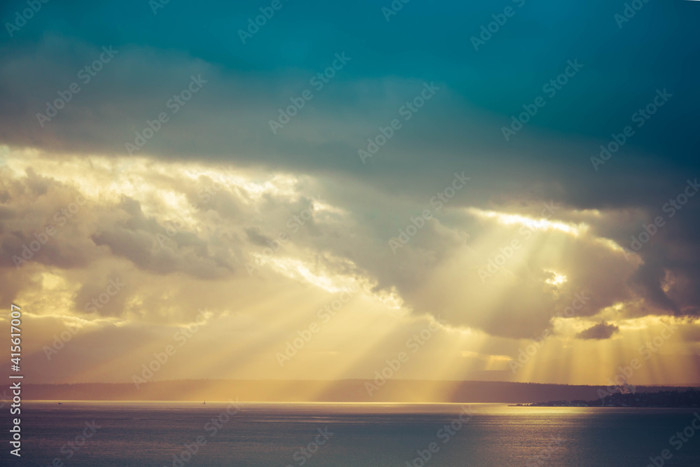 A dramatic sunset through the clouds over the ocean with rays of light piercing the clouds.