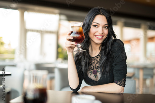 Pretty dark haired woman lookingat camera and drinking coke photo
