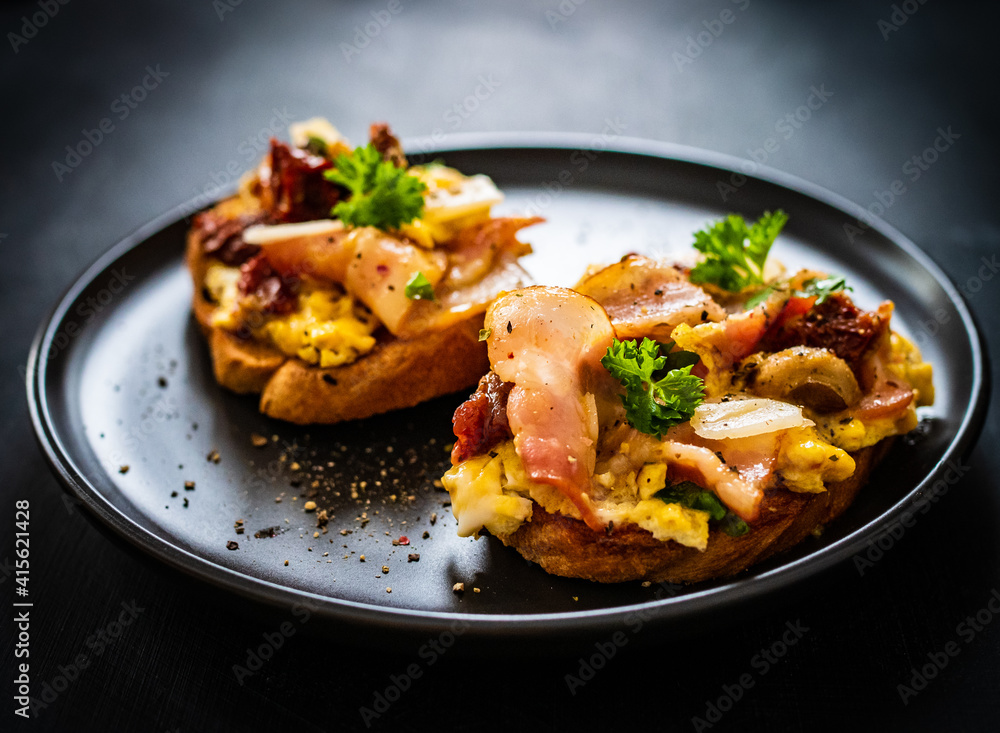 Delicious breakfast - scrambled eggs with bacon and champignons and sun-dried tomatoes on toasted bread on black table
Delicious breakfast - scrambled eggs with bacon and champignons and sun-dried tomatoes on toasted bread on black table