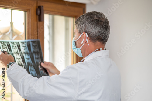 Doctor wearing face mask looking at x-ray backlit at the room window © jovannig