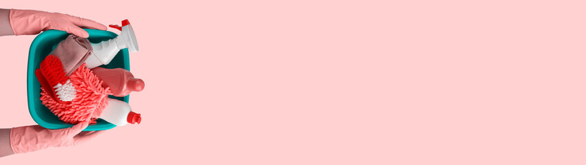 Hands in rubber gloves hold a basin with cleaning supplies isolated on pink background with place for text banner
