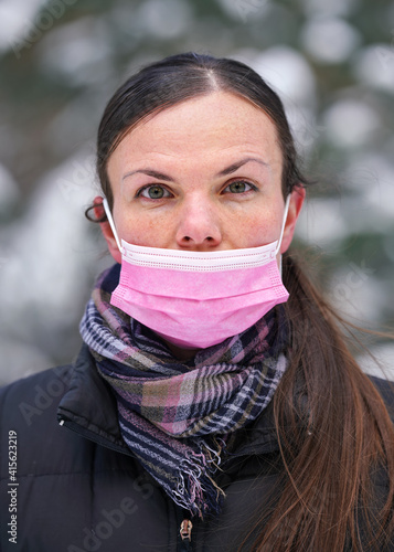 Foto Young woman in warm winter clothing wearing pink disposable virus face mask inco