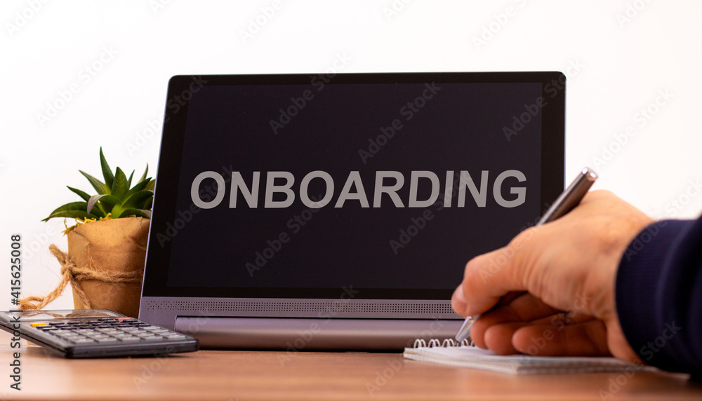 E-business and onboarding symbol. Tablet with the word 'onboarding'. Online business and onboarding during COVID-19 quarantine. Businessman hand with pen, house plant. Copy space. Onboarding concept. E-business and onboarding symbol. Tablet with the word 'onboarding'. Online business and onboarding during COVID-19 quarantine. Businessman hand with pen, house plant. Copy space. Onboarding concept.