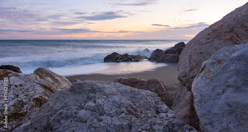 A picturesque scene of the sunset above sea waters seen through the rocky shore