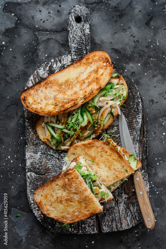 Sandwiches with turmeric fried chicken, cucumber, microgreens and homemade mustard mayonnaise sauce on a wooden cutting board on a dark background. Delicious tapas, snack, breakfast