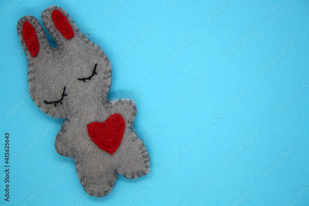 A bunny made of gray felt with a red heart.
