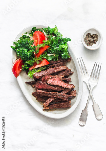 Beef steak and kale, tomato salad - delicious balanced diet lunch on a light background, top view