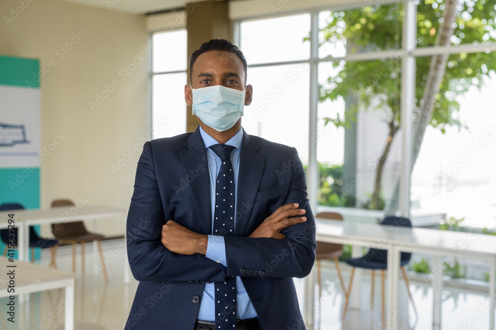 African businessman with surgical medical mask for protection with arms crossed at office looking at camera with arms crossed