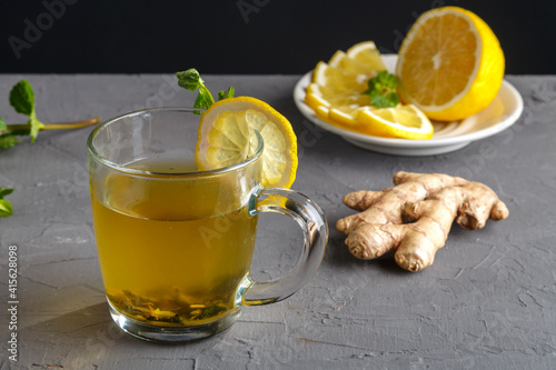 vitamin ginger drink with honey mint and lemon in a glass cup near ginger root and lemon on a concrete background.