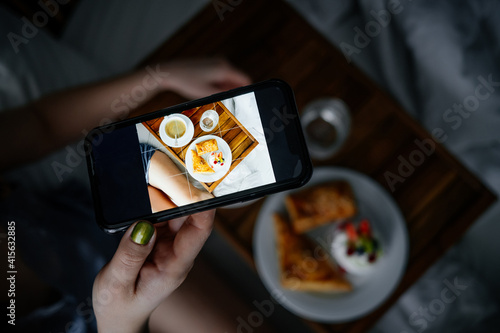 Female taking picture of a cup of coffee and delicious pastries on a board on her bed